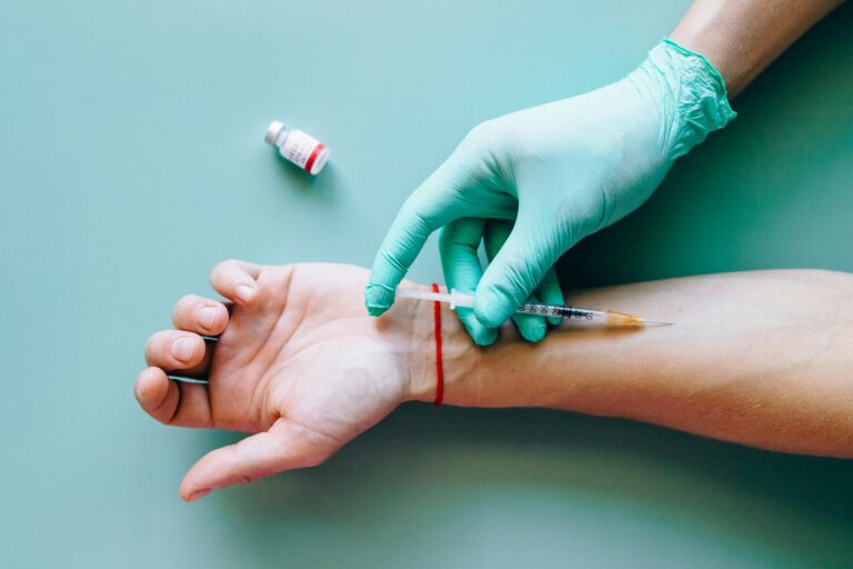Close-up of a medical syringe being applied to an arm by a gloved hand.