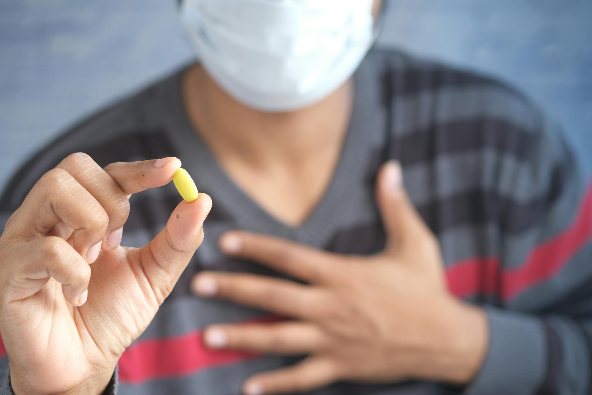 Close-up of a person wearing a mask holding a yellow pill, demonstrating healthcare emphasis.