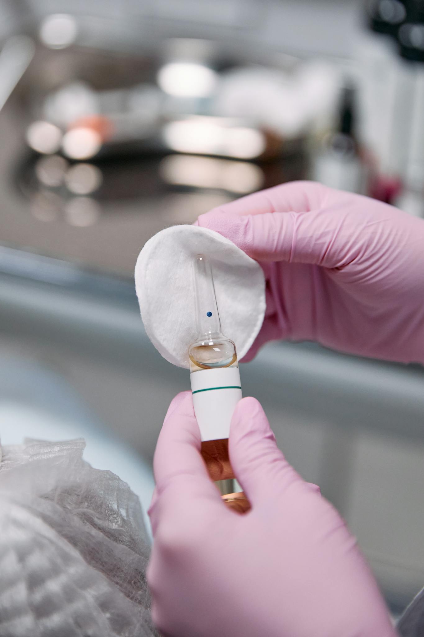 Close-up of hands in latex gloves holding a medical ampoule with cotton pad.
