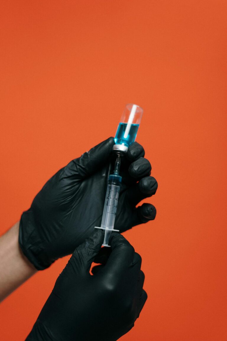 Close-up of hands with black gloves preparing a syringe against orange background.