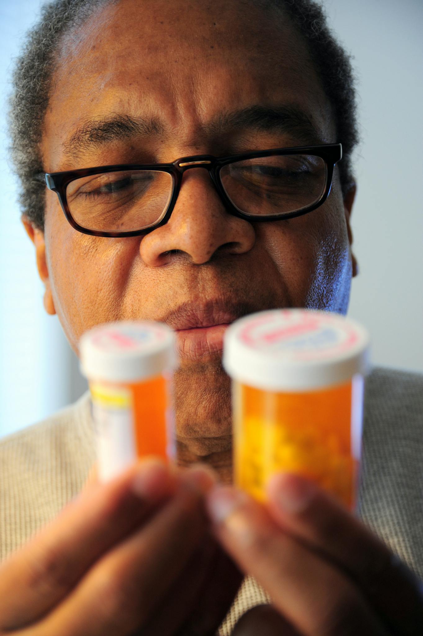 Senior adult man carefully examines two prescription pill bottles indoors.